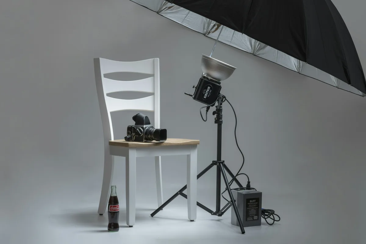 Equipo de estudio fotográfico con cámara sobre trípode y un paraguas difusor montado junto a una silla